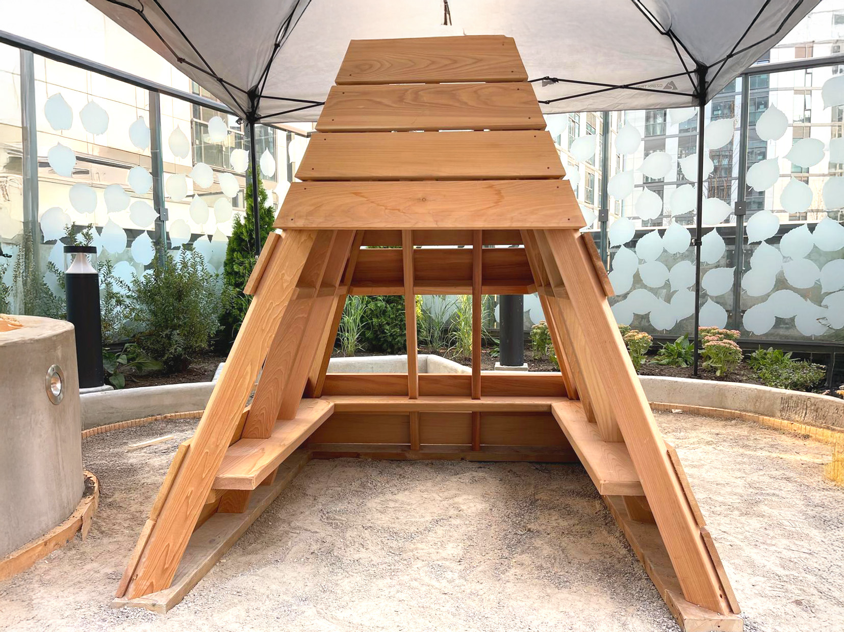 Custom A-frame seating structure in a glass-enclosed courtyard.
