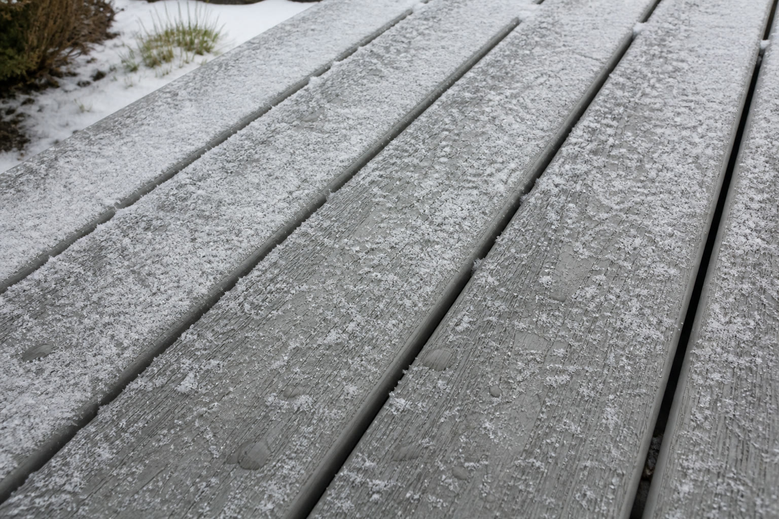 Snow-dusted composite deck boards showing the textured surface and drainage gaps