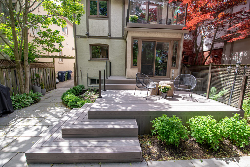 Two-level backyard deck with clear glass railings and composite decking
