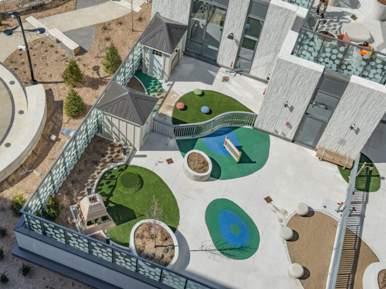 Aerial view of a modern outdoor playground with artificial turf, benches, and play structures on a rooftop terrace.