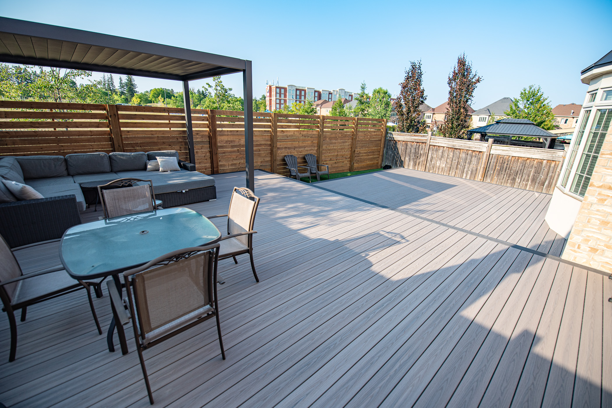 Spacious backyard deck with patio furniture, seating area under a canopy, and wooden privacy fence on a sunny day.