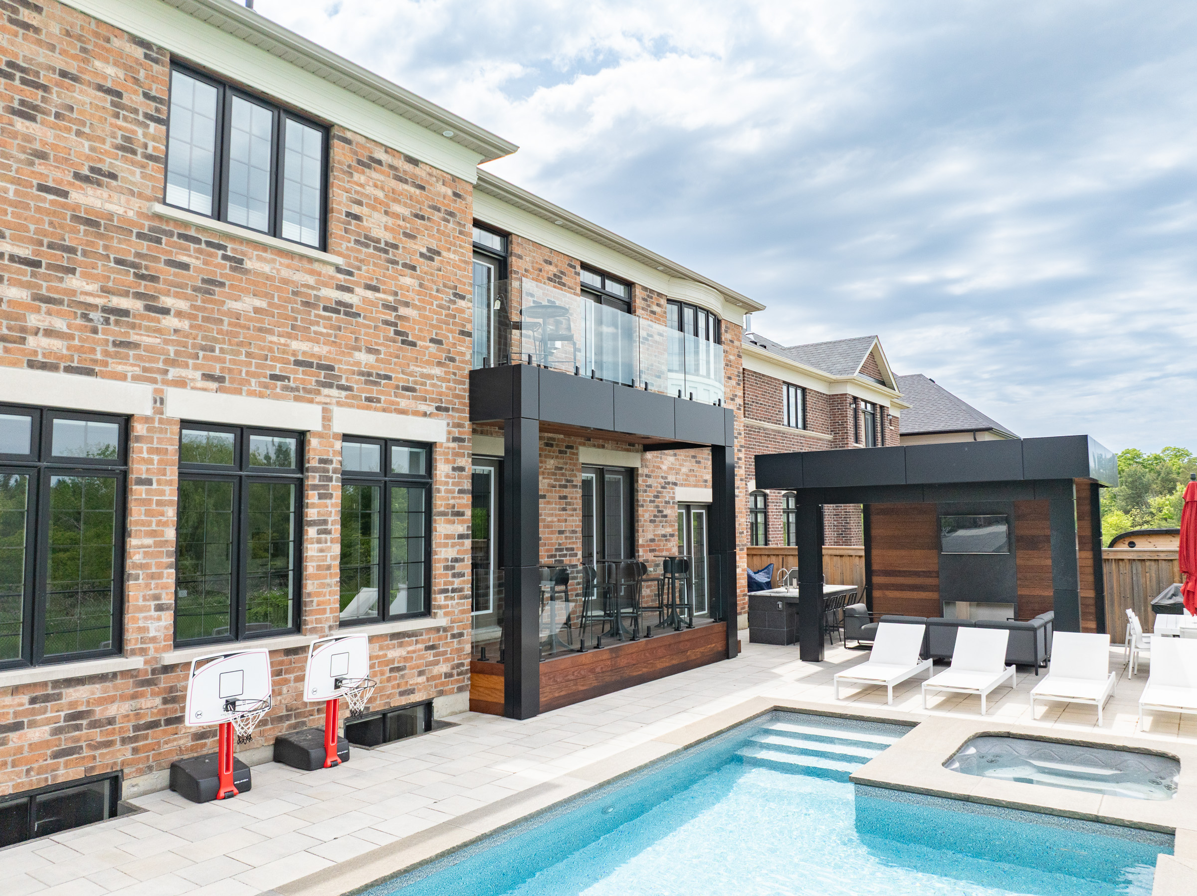 A modern backyard with a pool, hot tub, lounge chairs, patio seating area, and dining table with a red umbrella.