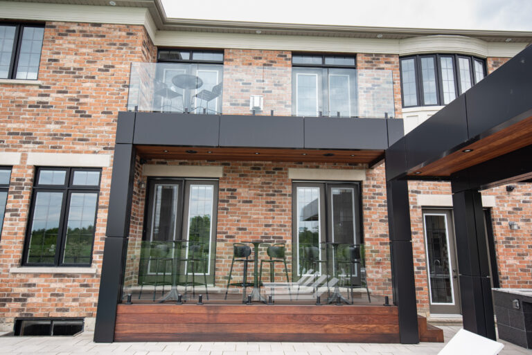 Modern brick house exterior with two levels of glass-railed balconies and black-framed windows and doors.