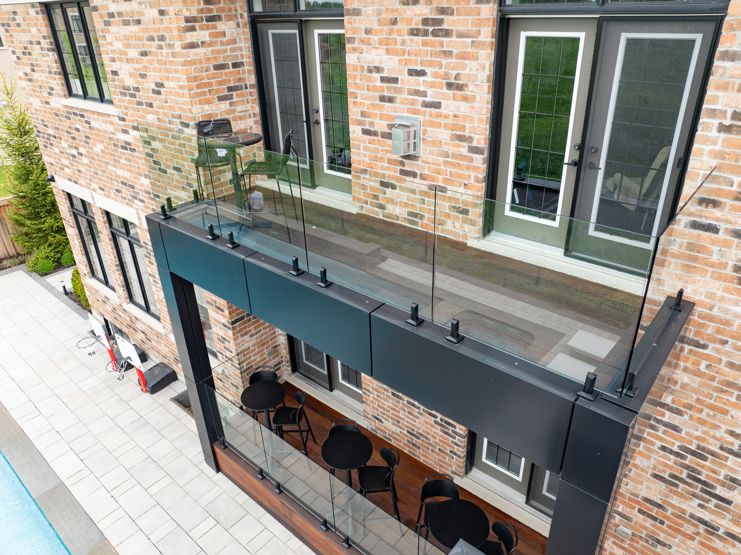 A modern brick building with a glass balcony above a patio area with tables and chairs beside a pool.