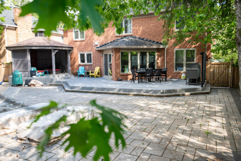 Wide view of the Richmond Hill backyard with a grey composite deck connecting the home, gazebo and stone patio
