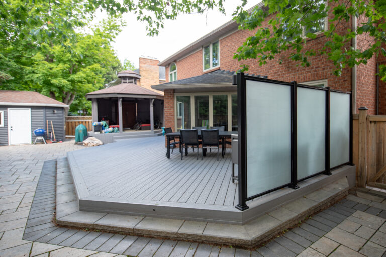 Angled view across the Fiberon Cottage deck toward the gazebo and black-framed frosted glass privacy screen