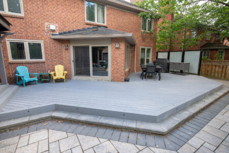 Grey composite deck wrapping the brick sunroom with a dining area and frosted glass privacy panels