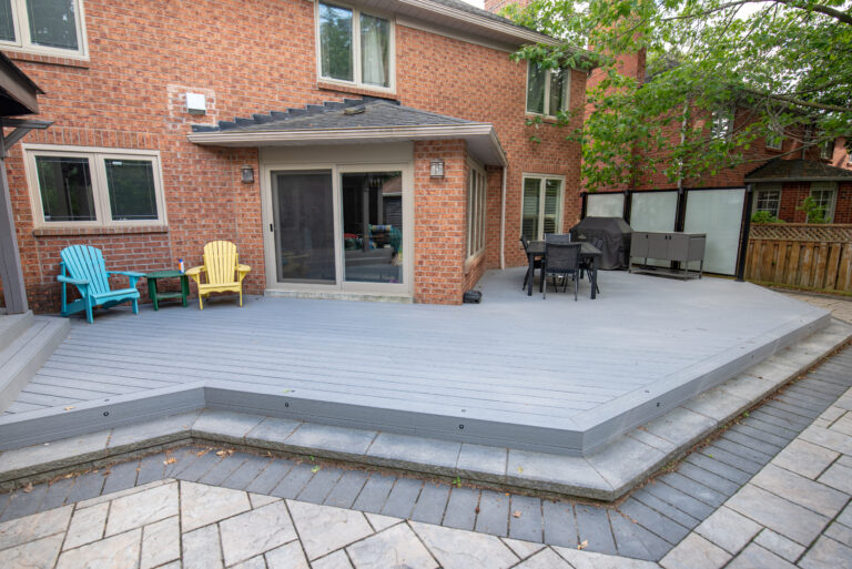 Grey composite deck wrapping the brick sunroom with a dining area and frosted glass privacy panels